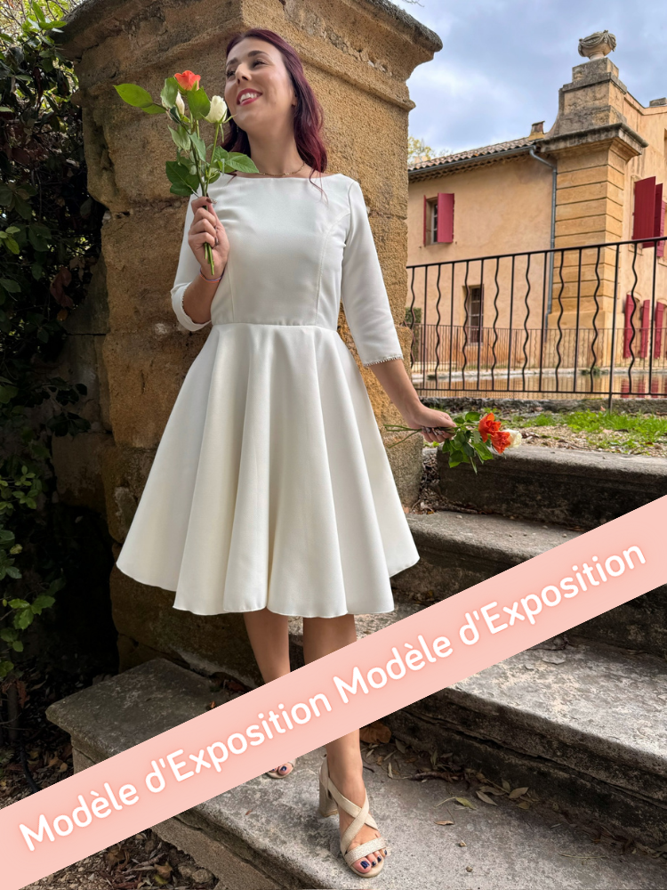 CASTOR Une robe de mariée civile en piqué de coton, avec un col bateau et des manches 3/4, finement bordées d'un galon.
