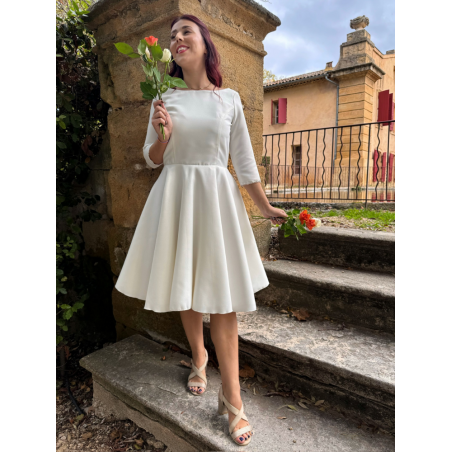 CASTOR Une robe de mariée civile en piqué de coton, avec un col bateau et des manches 3/4, finement bordées d'un galon.
